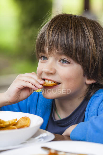 Retrato del niño sonriente comiendo papas fritas - foto de stock