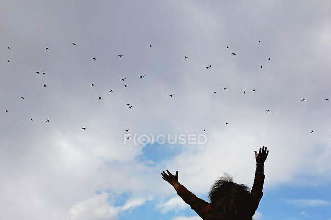 Silhouette de fille avec les bras tendus vers un troupeau d'oiseaux — Photo de stock