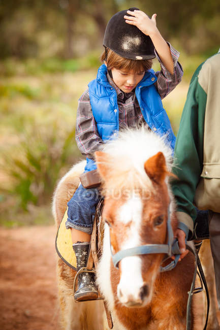 Retrato de menino usando capacete equitação cavalo de pônei — Fotografia de Stock