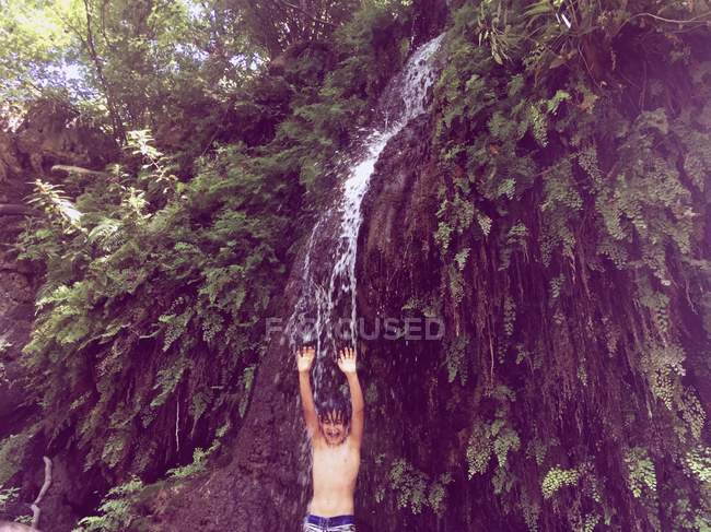 Хлопчик стоїть під водоспадом влітку — стокове фото