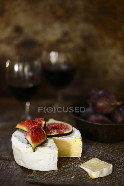 Свині та сир на дерев'яному столі з двома розмитими келихами вина на фоні — стокове фото