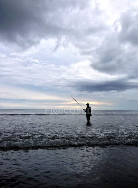 L'homme pêche dans l'océan sous un ciel nuageux — Photo de stock