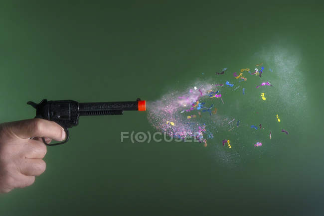 Mano masculina disparando una pistola de fiesta de juguete con confeti sobre fondo verde - foto de stock