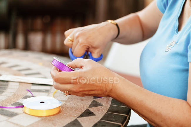 Imagen recortada de la mujer cortando cinta de colores sobre la mesa - foto de stock