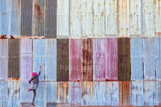Chica saltando delante de una pared de metal corrugado colorido - foto de stock