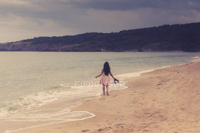 Вид ззаду дівчини, що йде піщаним пляжем — стокове фото