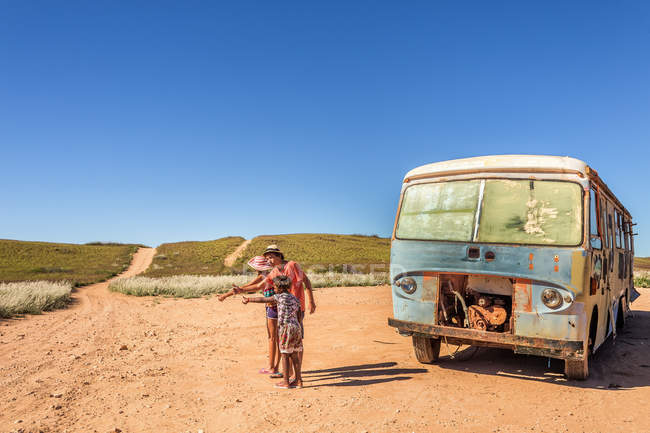 Three children hitchers at desert beside old damaged bus — Stock Photo