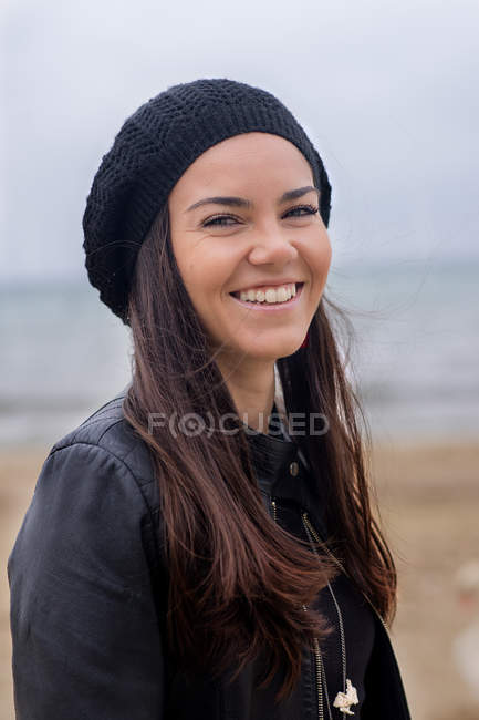 Ritratto di una donna sorridente con un cappello nero sulla spiaggia — Foto stock