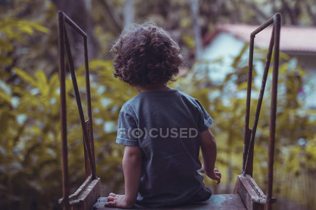 Visão traseira do menino bonito com cabelo encaracolado sentado em um slide — Fotografia de Stock
