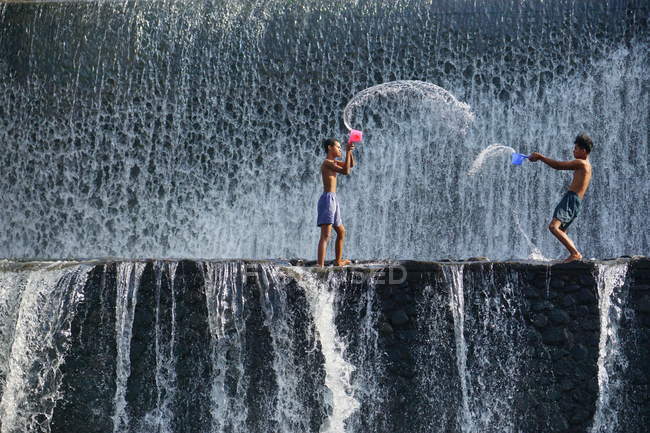 Dos chicos lanzándose agua entre sí, Tukad Unda Dam, Bali, Indonesia - foto de stock