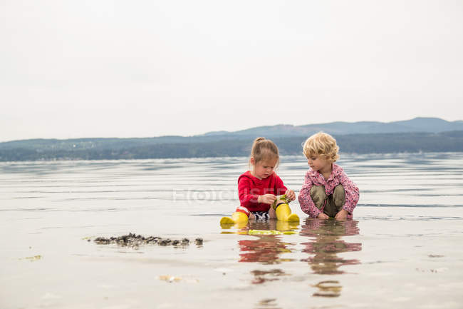 Zwei süße Schwestern sitzen auf Sand und spielen am Strand — Stockfoto