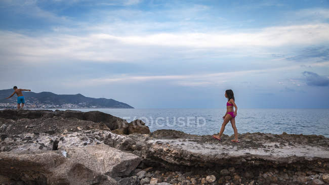 Due bambini che camminano lungo la spiaggia rocciosa, Barcellona, Spagna — Foto stock
