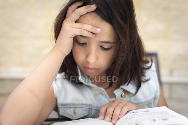 Close-up of girl reading book with hand on head — Stock Photo