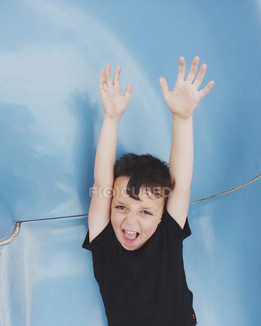 Niño con los brazos levantados y la boca abierta mirando a la cámara - foto de stock