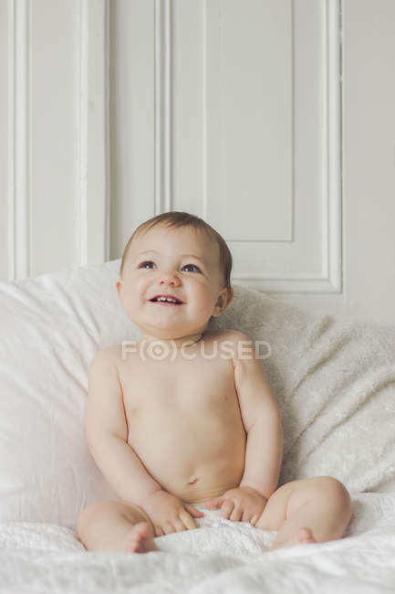 Retrato del niño sonriente sentado en la cama en el dormitorio - foto de stock
