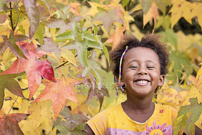 Retrato de niña sonriente en árbol colorido en otoño - foto de stock