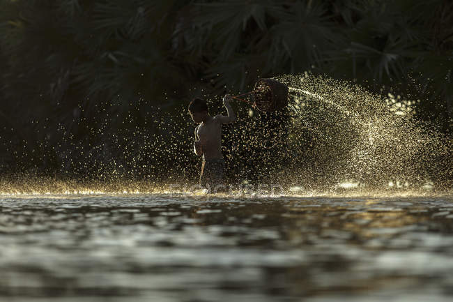 Silhouette di ragazzo spruzzi d'acqua con cesto nel fiume — Foto stock