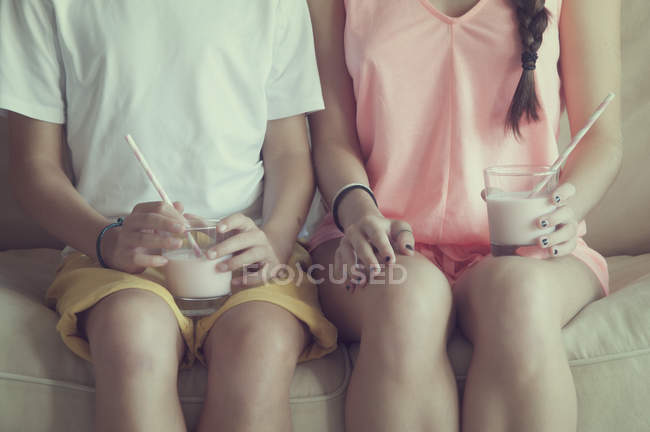 Cropped view of boy and girl sitting on sofa with glass of milk — Stock Photo