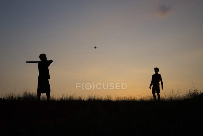 Silhouette zweier Jungen, die bei Sonnenuntergang Baseball spielen — Stockfoto