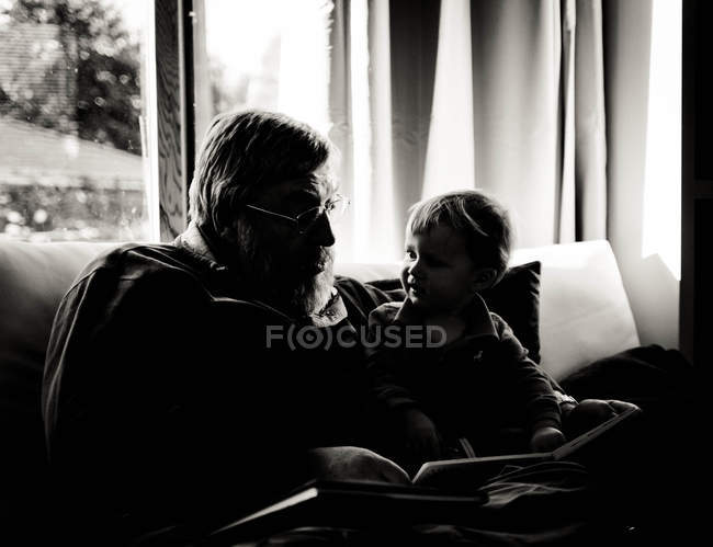 Silhouette of grandfather reading to his grandson at home — Stock Photo