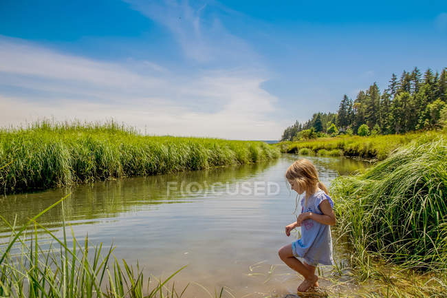 Chica rubia vistiendo vestido de verano caminando en el río - foto de stock