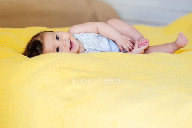 Sorrindo bebê menina deitada em uma cama — Fotografia de Stock
