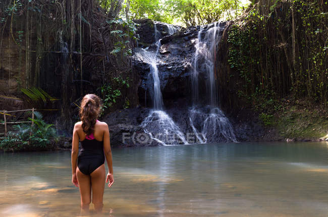 Vista trasera de la joven en traje de baño de pie en la piscina natural - foto de stock