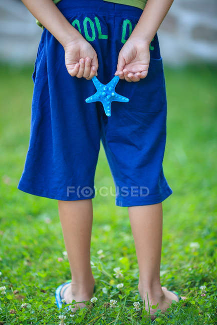 Low section of a boy holding starfish behind back — Stock Photo