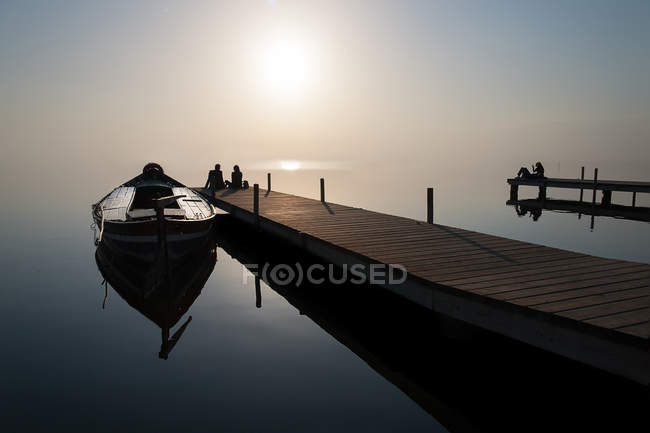 Silhouette de couple assis à la fin de la jetée par bateau amarré — Photo de stock