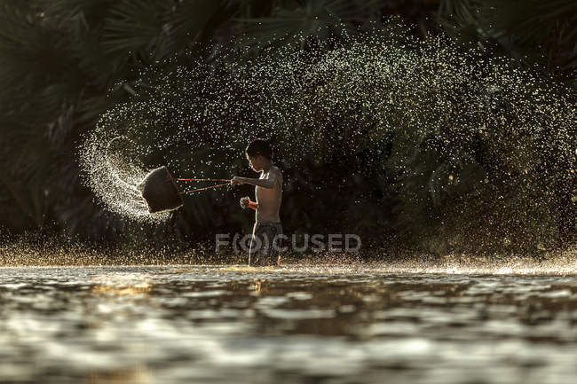 Menino segurando balde e espirrando no rio — Fotografia de Stock