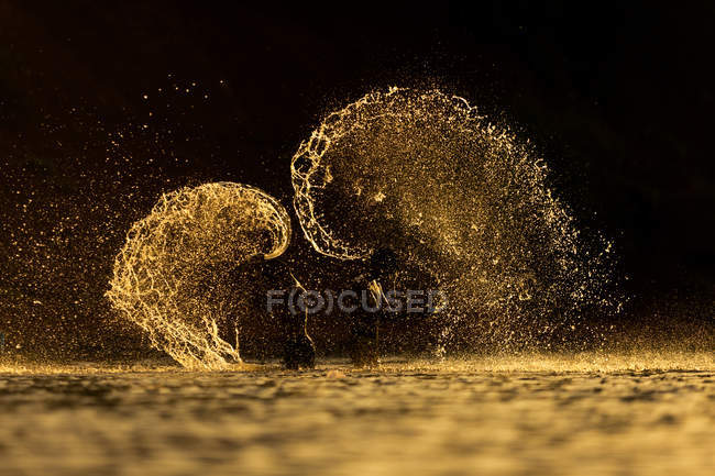 Image conceptuelle de deux personnes asiatiques dans des éclaboussures d'eau dorée — Photo de stock