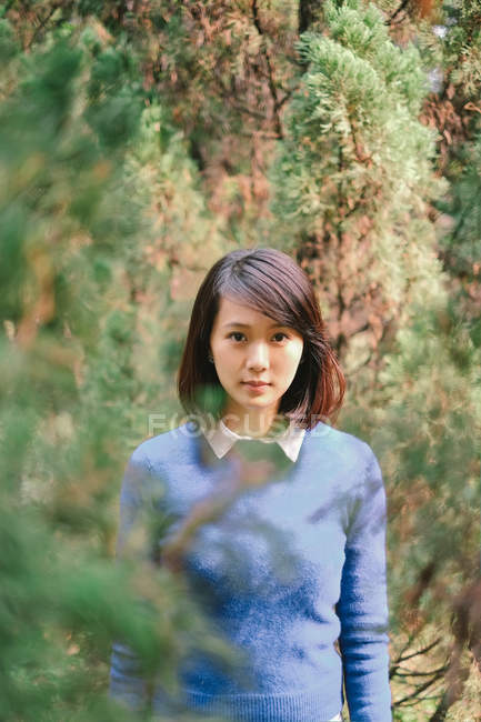 Porträt einer Frau, die zwischen Bäumen im Wald steht — Stockfoto