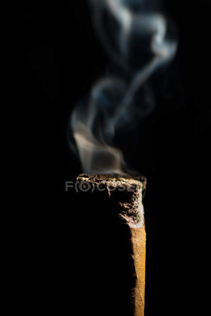 Close-up of a smoking cigar butt against black background — Stock Photo