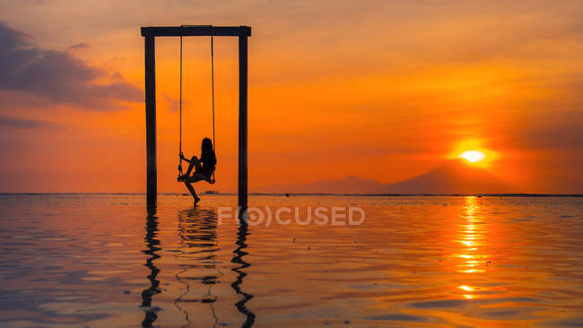 Silhouette einer Frau, die bei Sonnenuntergang auf einer Schaukel im Meer sitzt, Indonesien — Stockfoto