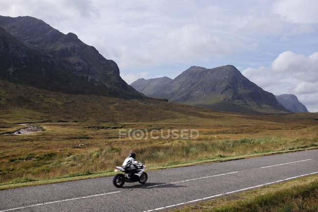 Мужчина на мотоцикле на дороге в горах, нагорье, Шотландия, США — стоковое фото