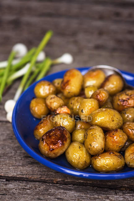 Batatas e cebolinhas em prato sobre mesa de madeira — Fotografia de Stock