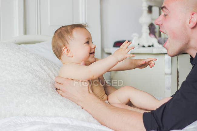 Vista lateral de feliz padre jugando con adorable bebé hijo - foto de stock