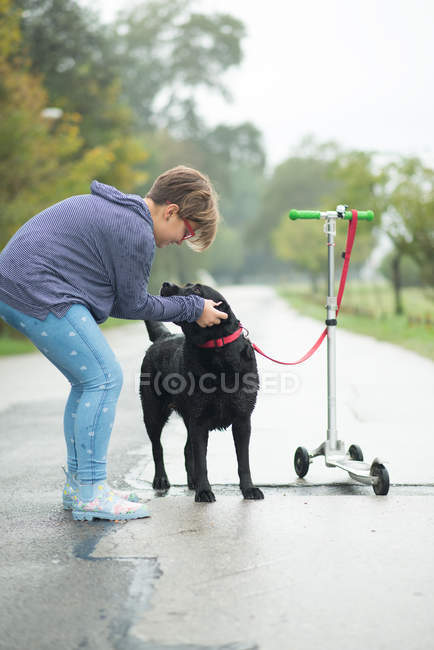 Chica acariciando perro atado a empujar scooter - foto de stock