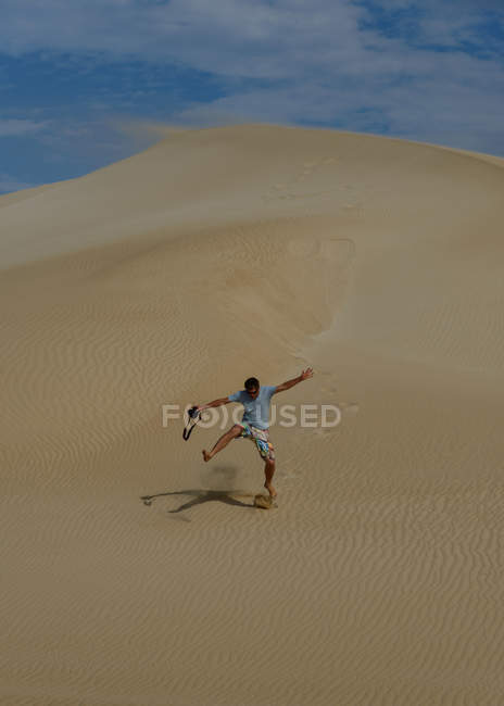 Man running down sand dune with cloudy sky on background — Stock Photo