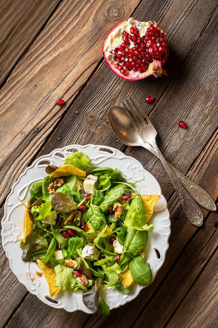 Pomegranate with green salad over wooden table, top view — Stock Photo