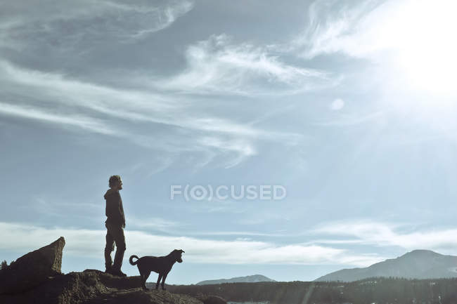 Hombre de pie sobre roca con perro y mirando a la vista, Estados Unidos, Colorado, Condado de El Paso, Pikes Peak - foto de stock