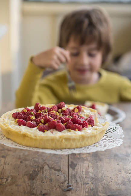 Torta de morango caseiro na mesa de madeira com menino comendo peça no fundo — Fotografia de Stock