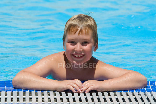 Ritratto di ragazzo sorridente appoggiato sul bordo della piscina — Foto stock