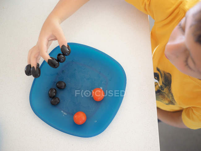Junge spielt mit Essen auf Teller, legt Oliven auf Finger — Stockfoto