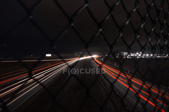USA, Indiana, Light trails at night through chain link fence — Stock Photo