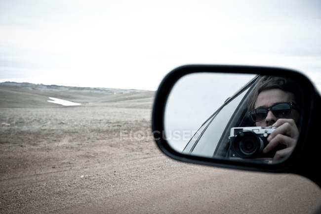 Frau mit Fotokamera reflektiert im Seitenspiegel von Auto — Stockfoto