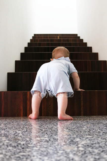 Vista trasera del niño subiendo escaleras de madera en el interior - foto de stock