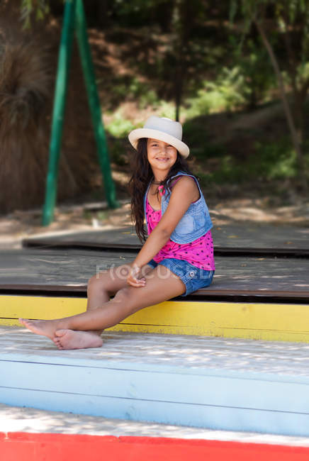 Девушка в шляпе сидит на красочной деревянной лестнице на открытом воздухе — стоковое фото