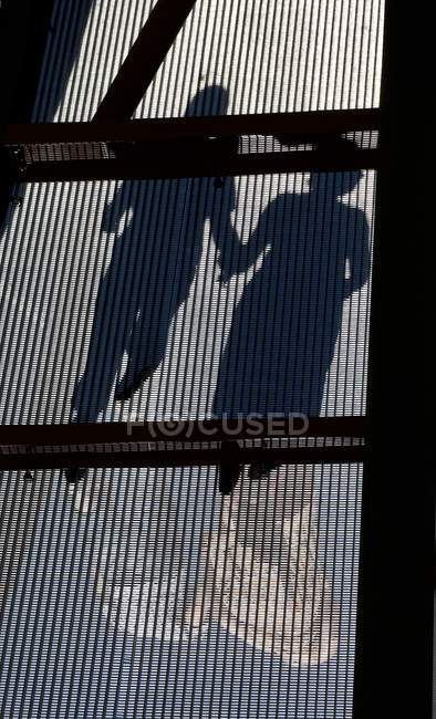 Schatten von zwei Menschen, die Händchen haltend über eine Brücke gehen — Stockfoto