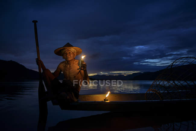 Hombre sentado en barco de pesca al atardecer, río Mekong, Tailandia - foto de stock